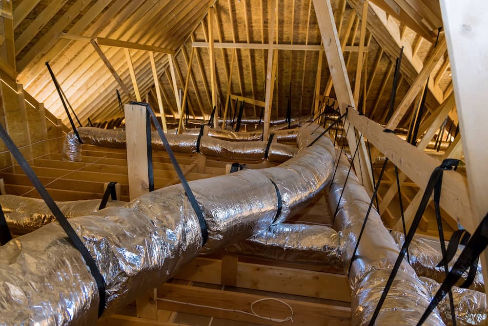 An expansive attic with wooden beams and reflective silver air ducts (properly size ductwork) secured by black straps ensures efficient airflow