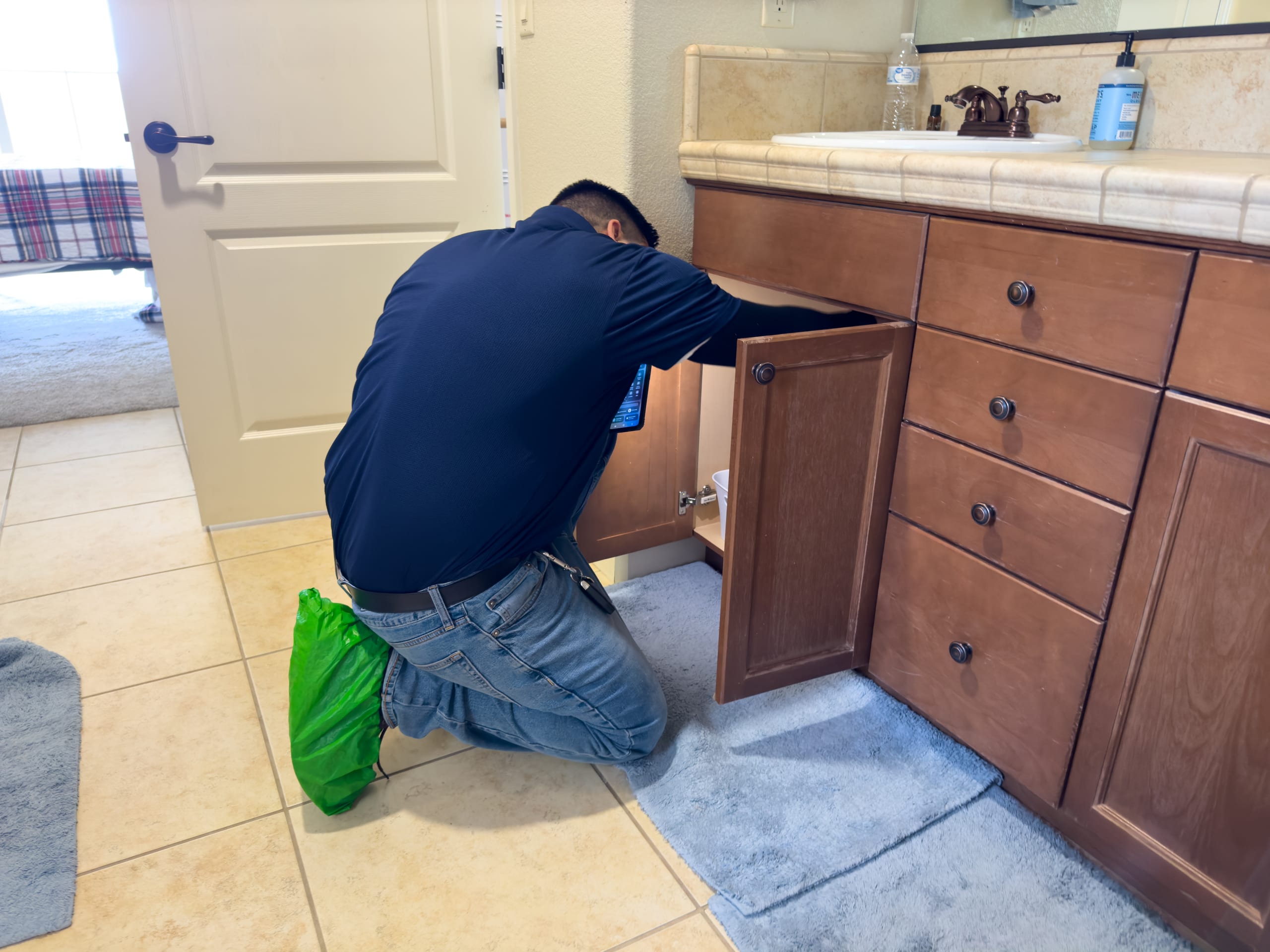 Plumber inspecting under bathroom sink for hidden leak damage