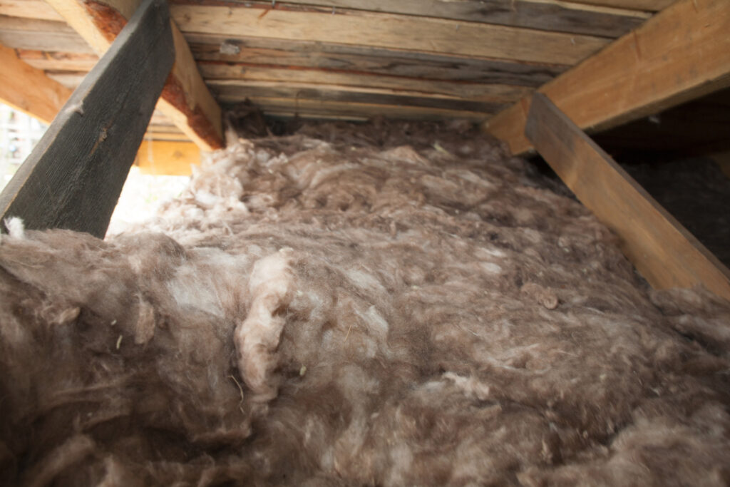 Fluffy brown sheep wool insulation fills a wooden attic space, showcasing sustainable building materials in the blown-in insulation vs batts comparison